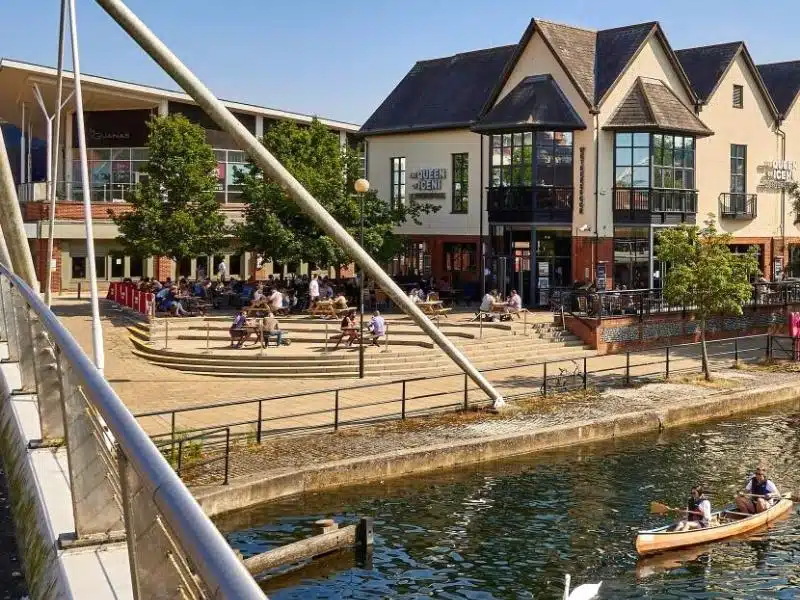 river with people canoeing and shops and a pub on the banks