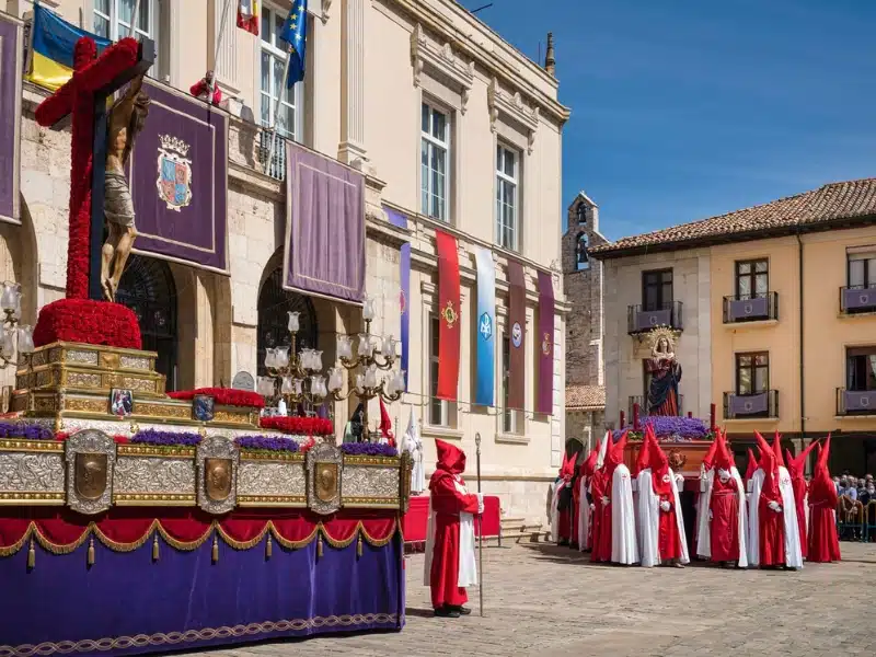 people wearing red and white costumes with red pointy hats by an Easter procession outside a church