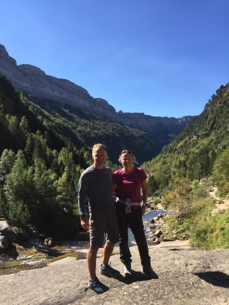 man and a woman in hiking gear standing in front of a river surrouned by trees