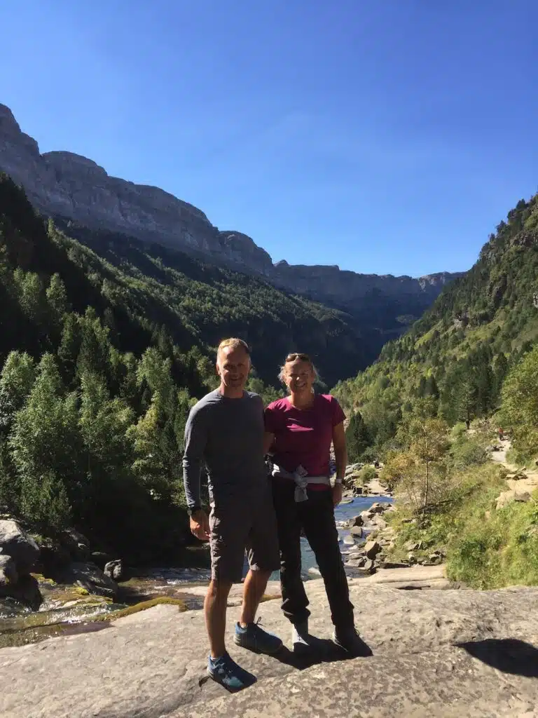 man and a woman in hiking gear standing in front of a river surrouned by trees