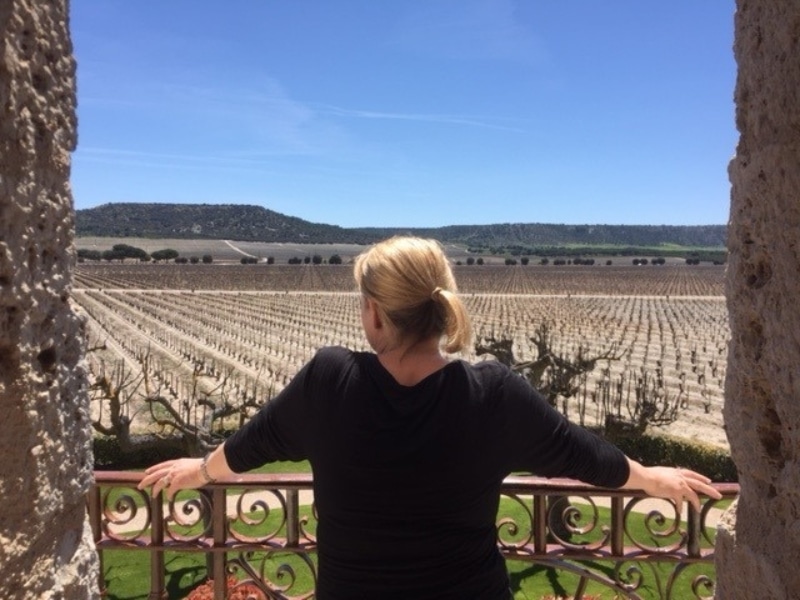 woman with a blond ponytail leaning on balcony railings over a vineyard