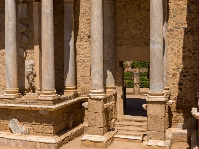 stone and marble Roman building with a headless statue and doorway to a green courtyard