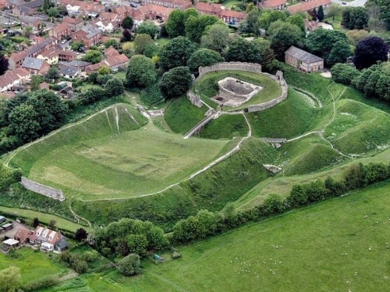 green meadows around ancient earthworks and a ruined castle