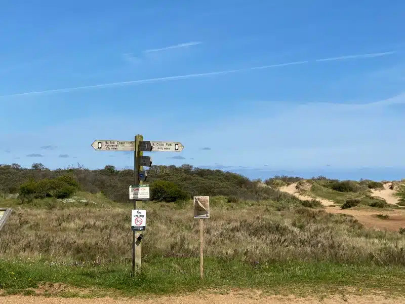 wooden signage on a sandy path with grassy dunes in the background