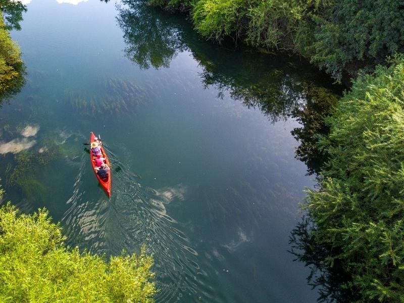 Red canoe with family paddle along a waterway lined with trees