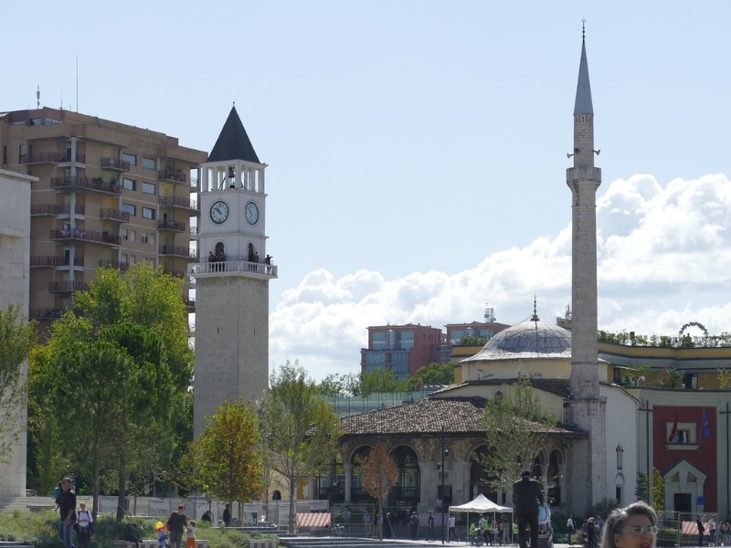 white minaret and stone clock tower surrounded by trees and other buildings