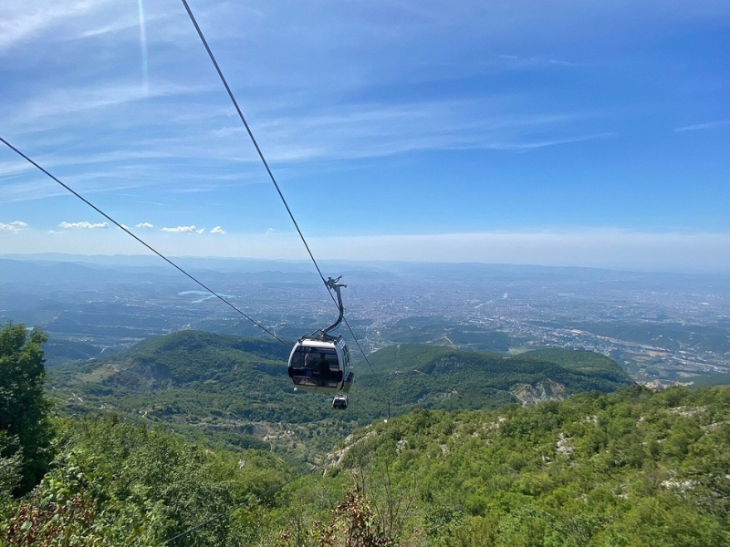 cable car about a hill covered in forest with a city in the distance