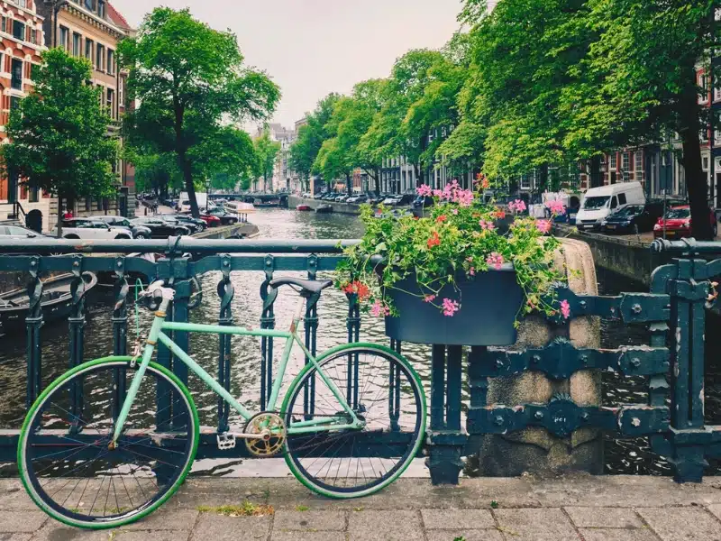 green bicycle resting against a bridge by a tub of pink flowers over a canal in Amsterdam