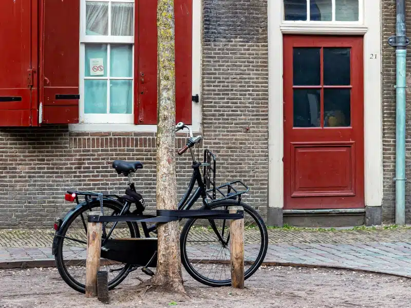 red brick house with red shutters and door and a black pike leaning againsta tree outside