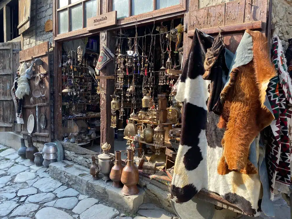 rugs and metalwork on display in a small shop on a cobbled street