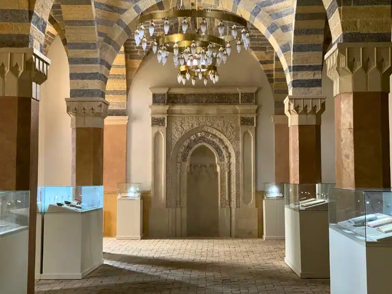 interior of historic building with cobbled floor, marble arches and a carver doorway. There are glass display cases between the columns.