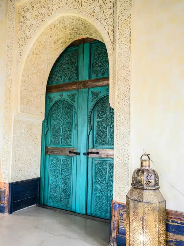 turquoise painted wooden door with intricate platerwork surrounding it and a traditional filigree lamp to the side