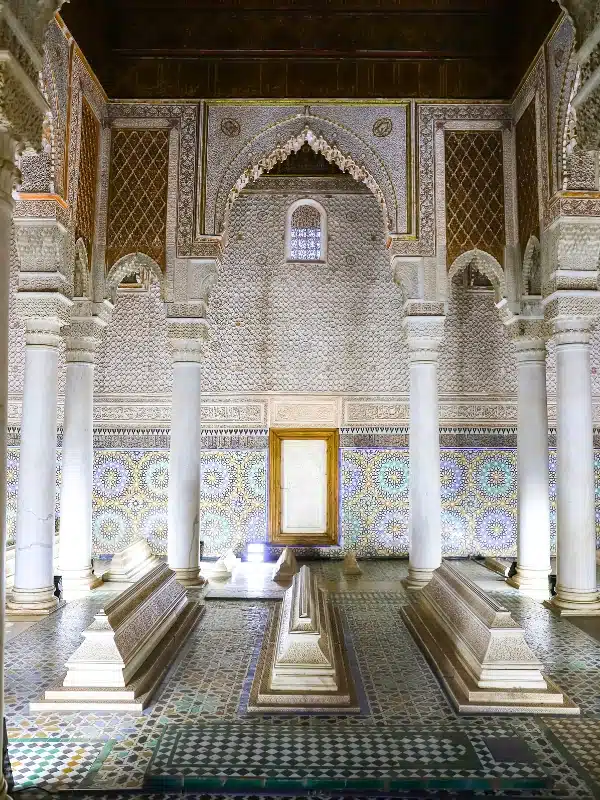 tiled toom with a wooden ceiling, marble columns and tombs on the floor.