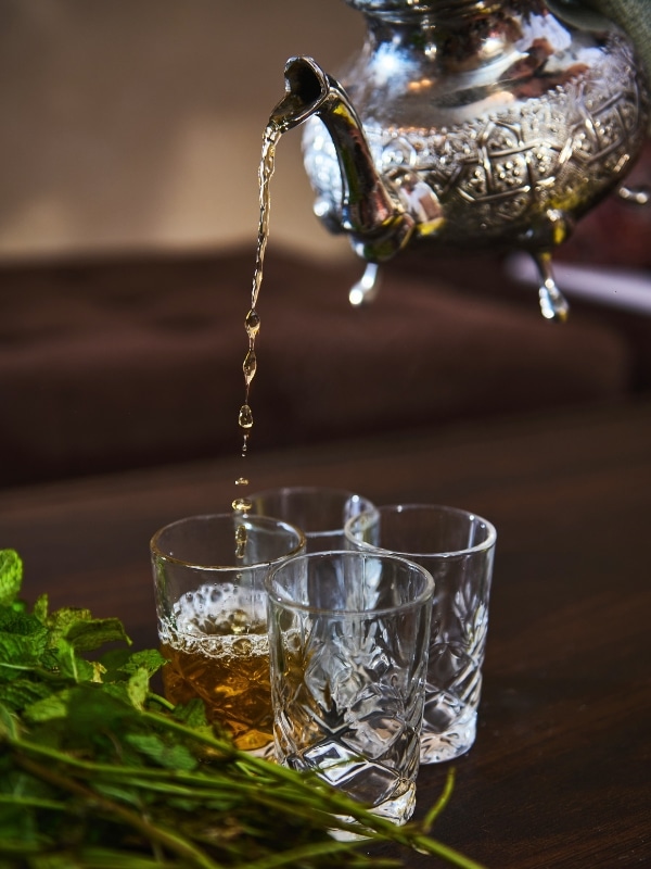 four glasses with Moroccan mint tea being poured into them from a silver tea pot
