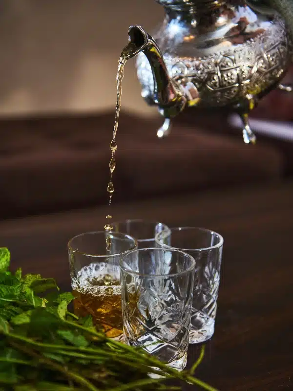 four glasses with Moroccan mint tea being poured into them from a silver tea pot