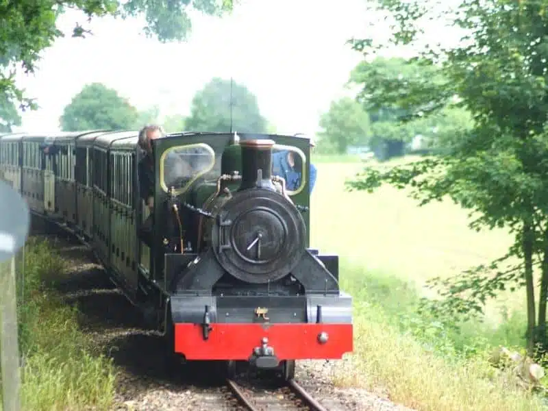 small steam train surrounded by green trees and fields