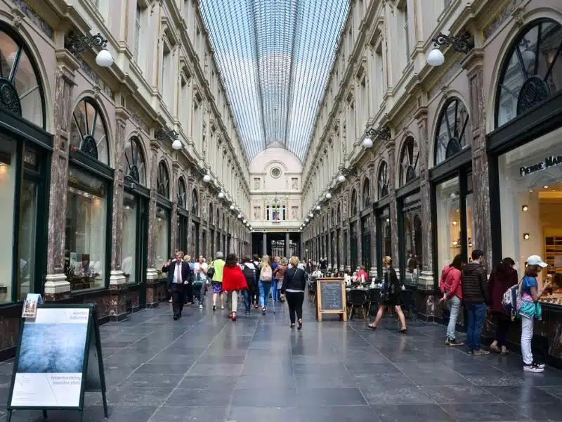 Ornate Victorian shopping arcade with glass roof and people window shopping