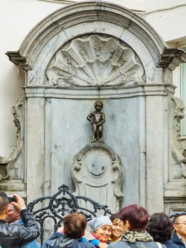 bronze statue of a small boy set in an ornate alcove with people taking photographs