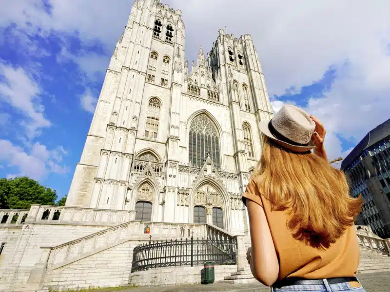 woman wearing a hat looking up at the twin spires of a large cathedral