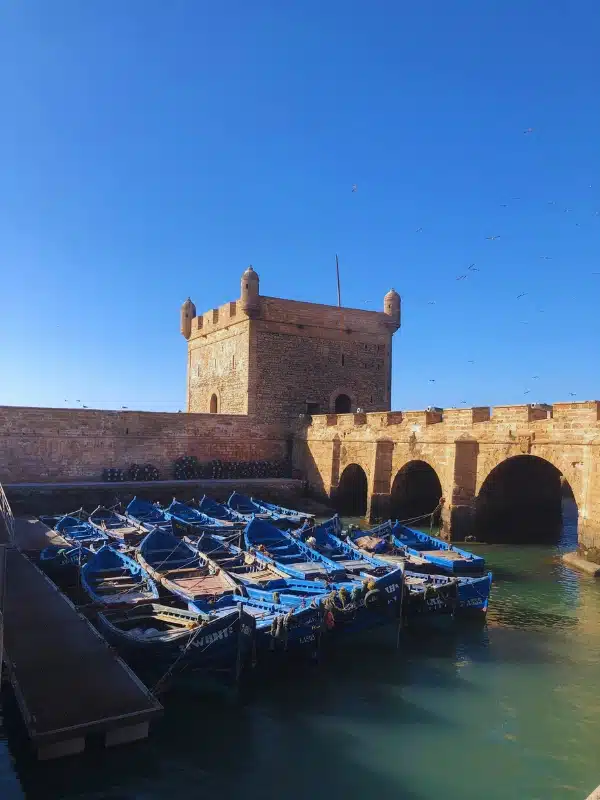 blue wooden fishing boats against a stone build tower and arched bridge