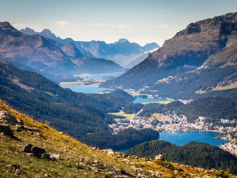 blue lakes seperated by a town surrounded by huge mountains