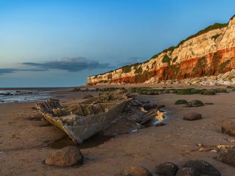 red and white striped cliffs with a ship wreck on the beach