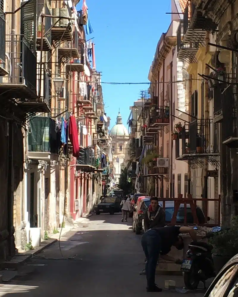 view down a colorful street with washing hanging from balconies and a domes church at the end