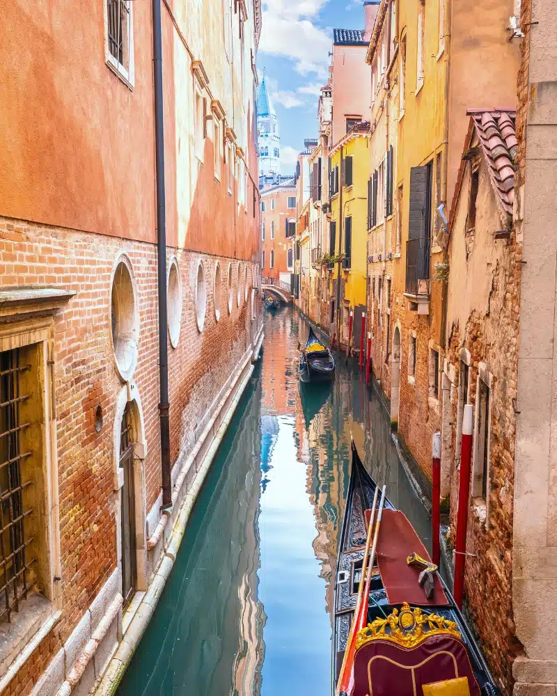 pink and yellow buildings lining a canal with gondolas in Venice