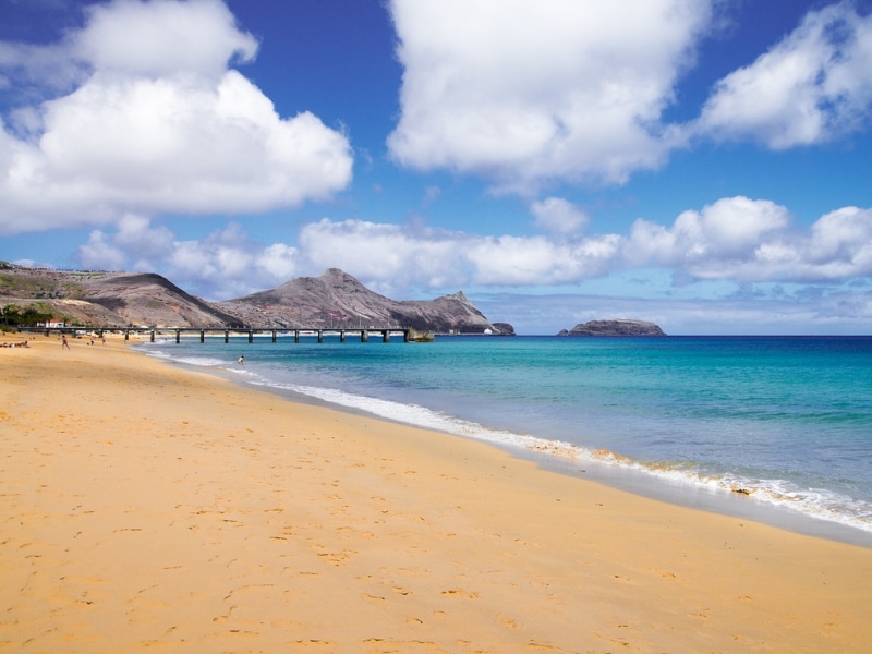 long stretch of sandy beach lapped by turquoise sea and mountains in the distance