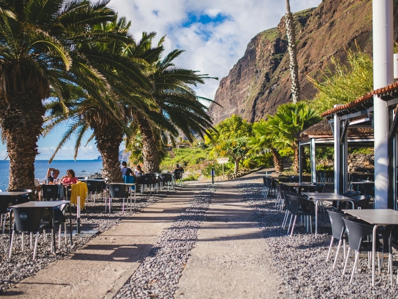 beach side restaurant with high cliffs in the background and tables and chairs outside