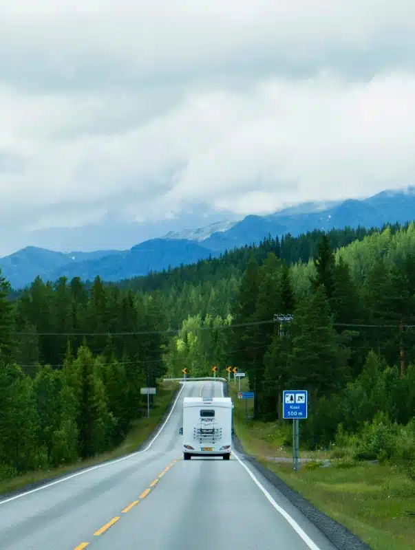 white motorhome on a road by a blue sign with mountains in could in the background