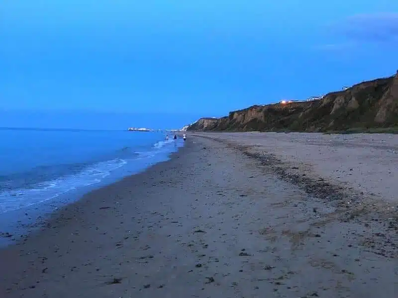 beach backed by small cliffs at dusk with some bilding lights shining 