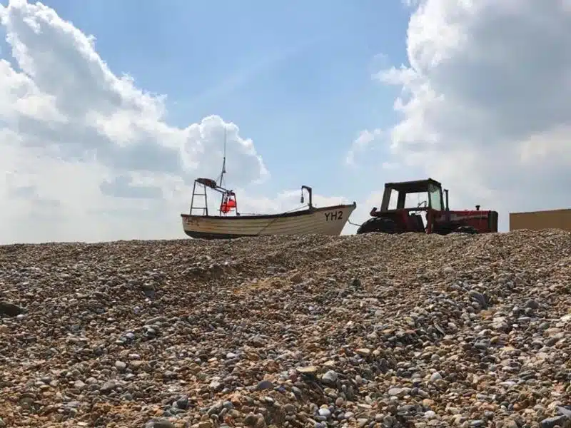 sloping pebble beach with tractor and wooden fishing boat at the top of the slope