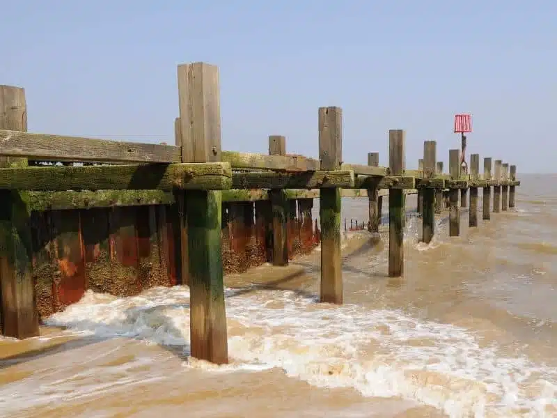 wooden groynes and a red marker jutting out to see from a beach