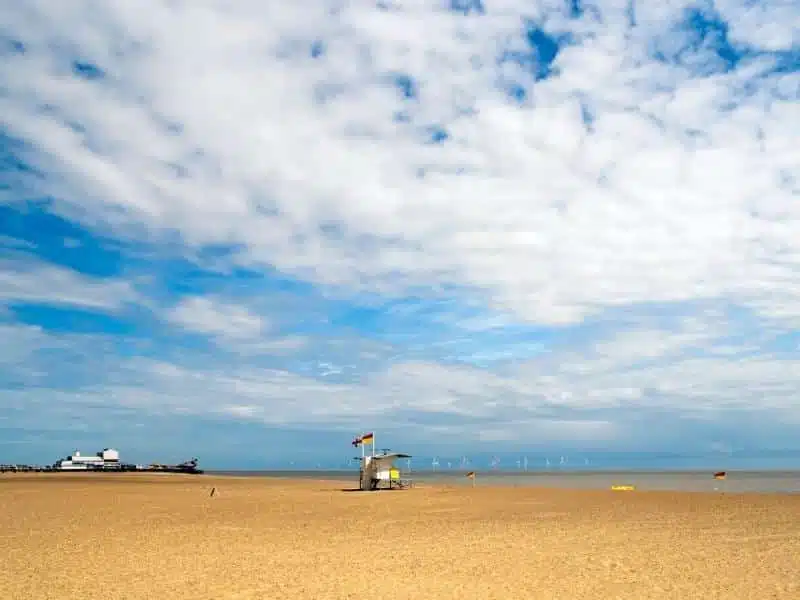 large beach with buildings in the far distance and a white lifeguard hut flying a red and yellow flag