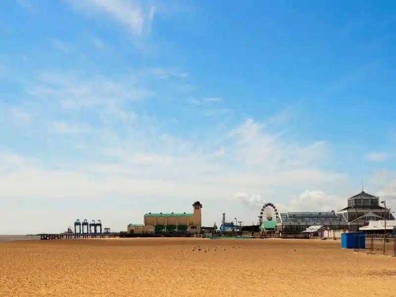 wide view of a beach with a fun fair and Ferris wheel in the distance