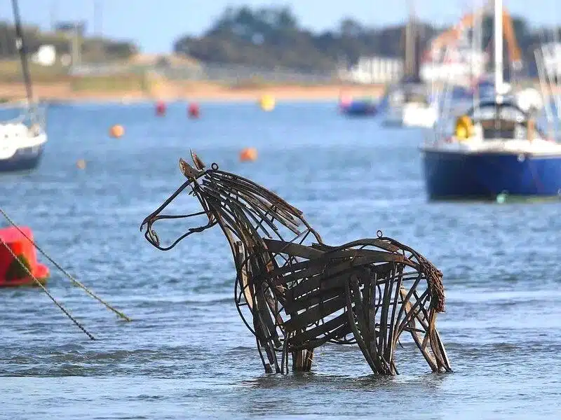 metal horse sculpture partially submerged in water and surrouned by boats