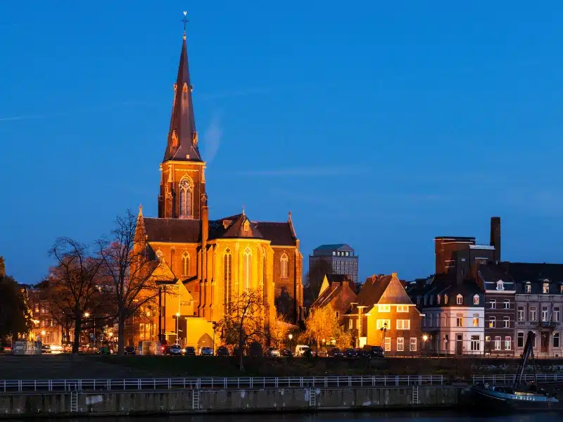 Church with an elegent tall spire and surrounding buldings lit up at night 