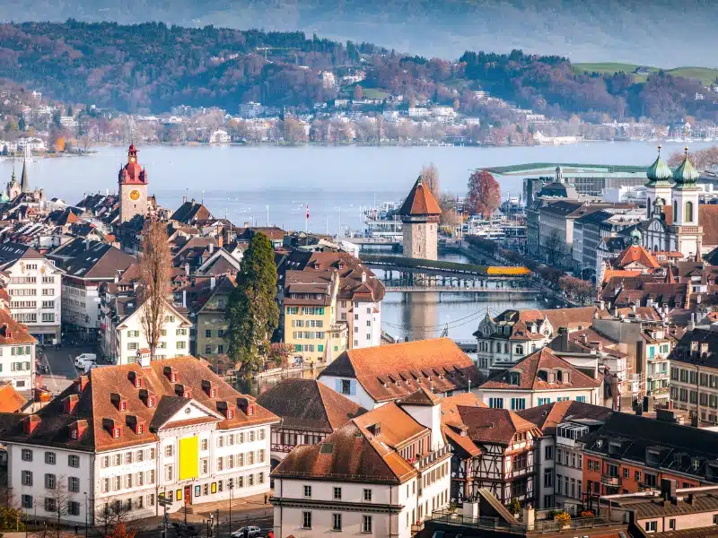 aerial view over a city of historic buildings and red roofs with a lake in the distance