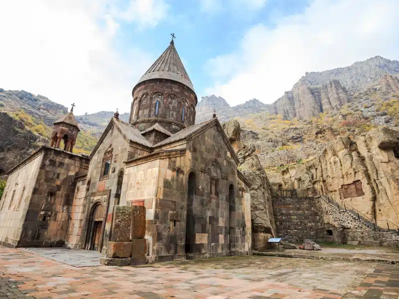 block built monastery with a conical roof with rock formations in the background