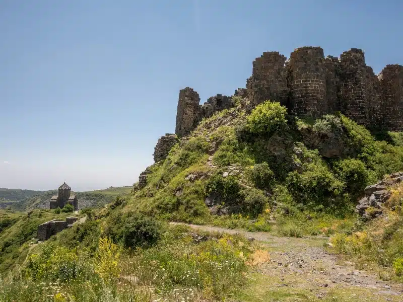 ruined fortress surrouned by lush greenery with a monastery in the background