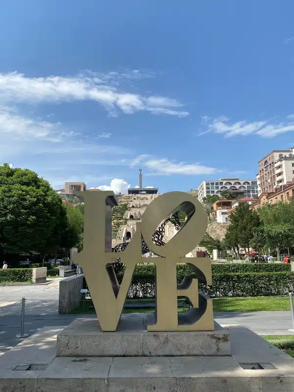 gold LOVE sign in a city surrounded by a park, staris and buildings