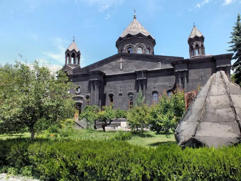 black stone church with three conical towers with trees and grass to the front of the building