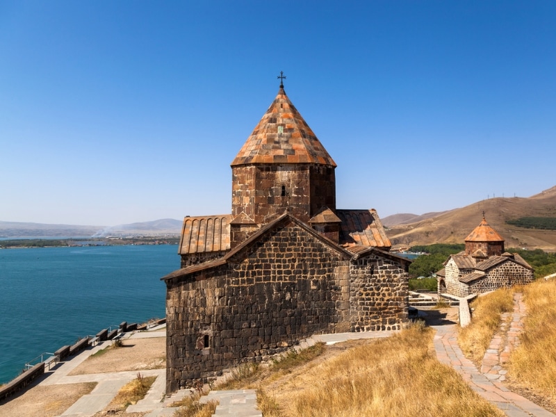 stone monastery with a conical roof with a turquoise lake in the background