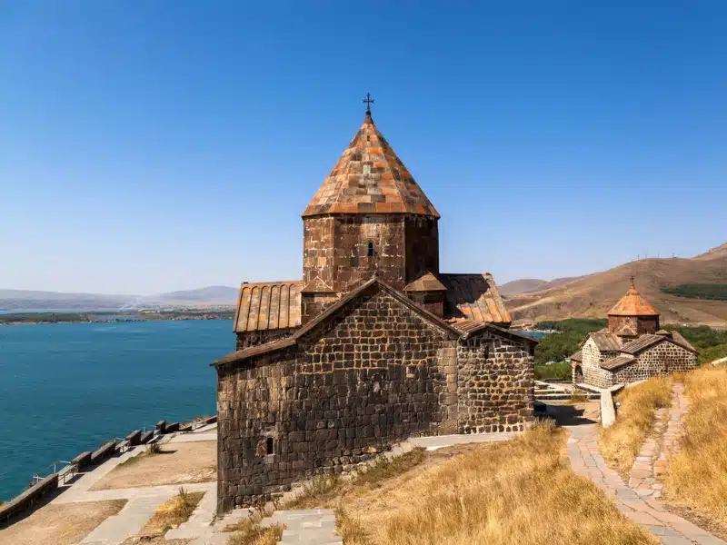 stone monastery with a conical roof with a turquoise lake in the background