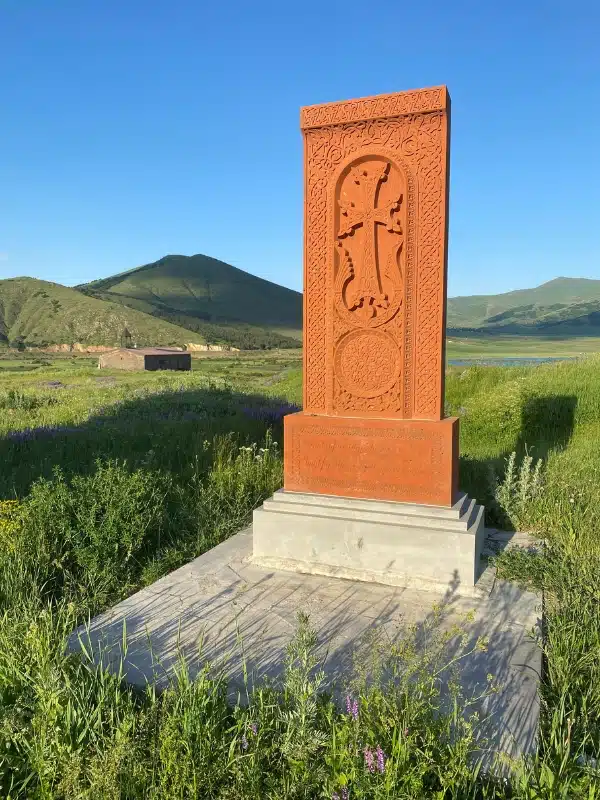 red standing stone carved with a cross and intircate designs, with a small chucrh un the background