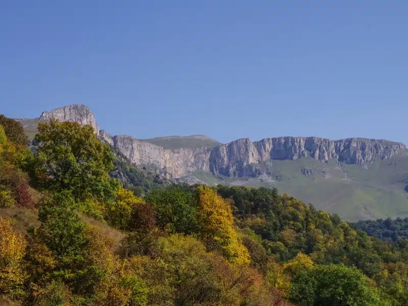 large rocky crags above green meadows and autumn trees