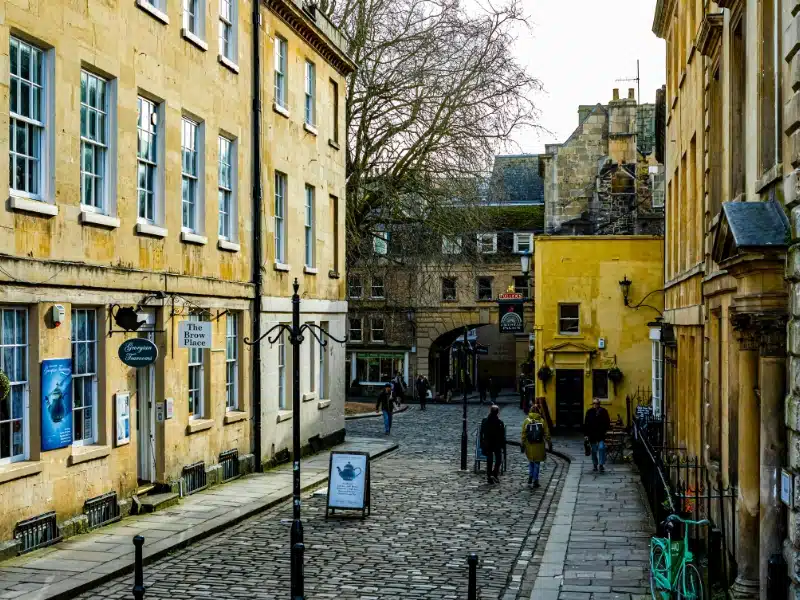 stone buildings lining a cobbled street with a stone archway in the background