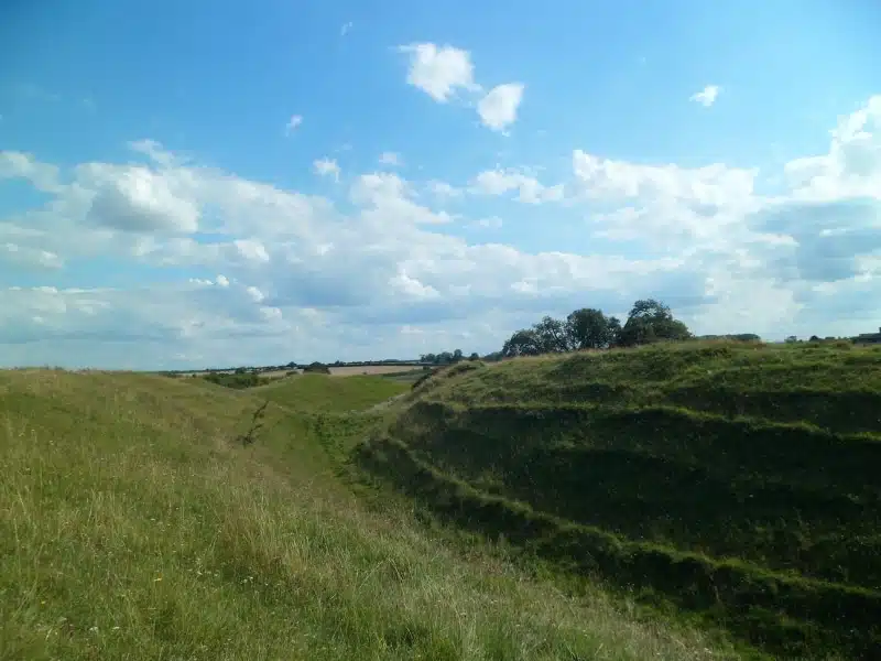 grass covered earth works from a ancient fort with trees in the distance