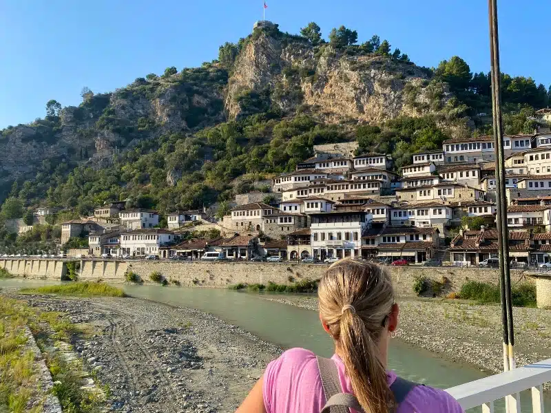 woman in a pink tshirt looking from a bridge to a group of white houses with many windows